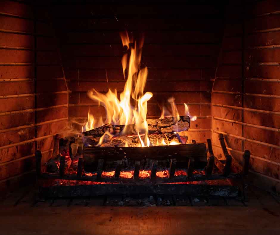 A warm fire burning with bright orange and yellow flames inside a brick fireplace, with logs resting on a metal grate. A warm fire burning with bright orange and yellow flames inside a brick fireplace, with logs resting on a metal grate.